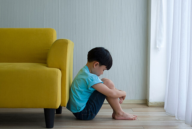 暗い部屋で足を抱えて座っている子供